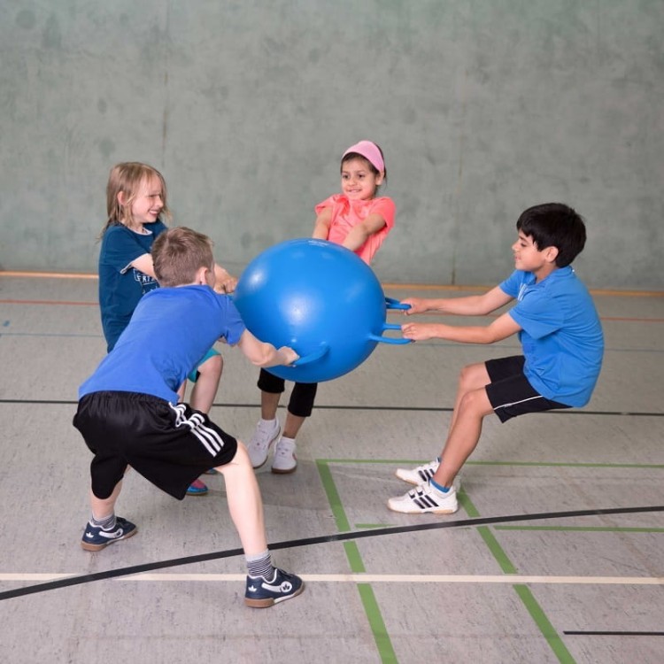 Dzieci bawiące się piłką Ring Ball podczas zajęć grupowych, obraz pokazuje zastosowanie w przedszkolu przy średnicy 55 cm