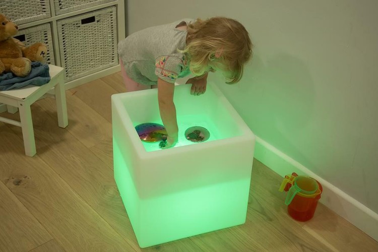 Stolik sensoryczny ustawiony w kąciku zabaw z materiałami do eksperymentów sensorycznych i elementami edukacyjnymi