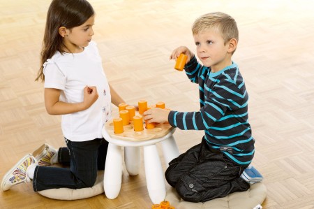 Pomarańczowe shakery ułożone na drewnianej podstawie gry pamięciowej Shake'n'Play, idealne dla dzieci od 3 lat