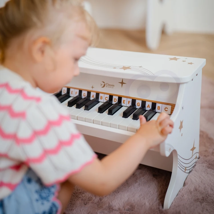 Otwarta książeczka do nauki obok pianina CLASSIC WORLD z widocznymi nutami i ilustracjami
