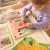 Ręka trzyma jedną pinezkę nad planszą — pokaz zastosowania układanki TOOKY TOY w praktyce