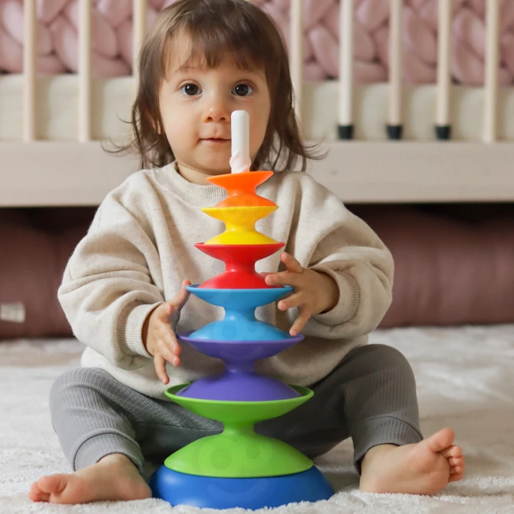 Zbliżenie na układanie krążków piramidki WOOPIE BABY — dziecięca ręka nakłada elementy, widoczna faktura powierzchni