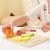 Elementy układanki rozłożone na stole — zestaw owoców, nóż i plansza VIGA Montessori w naturalnych kolorach