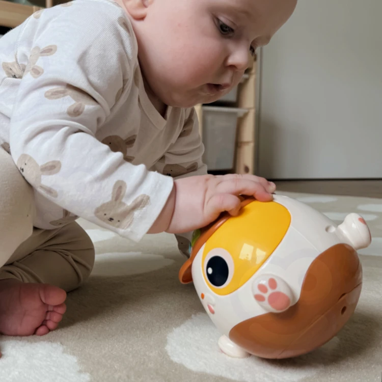 Niemowlę trzyma grającą kulę Piesek WOOPIE — ergonomiczny kształt i łatwy chwyt widoczne podczas zabawy