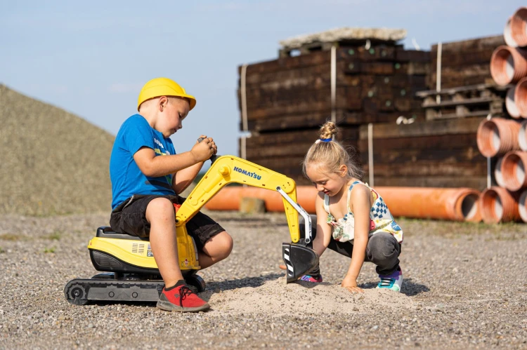Kask do zabawy ułożony obok koparki — widoczny pas regulacyjny i wykończenie, marka FALK