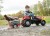 Widok z boku na traktor RollyJunior RT Rolly Toys — kierownica, pedały i przyczepa widoczne podczas jazdy