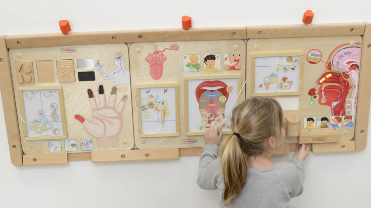 Dziecko bawi się Tablicą Edukacyjną Zmysł Dotyku — praktyczne ćwiczenia manualne na drewnianej zabawce Montessori.