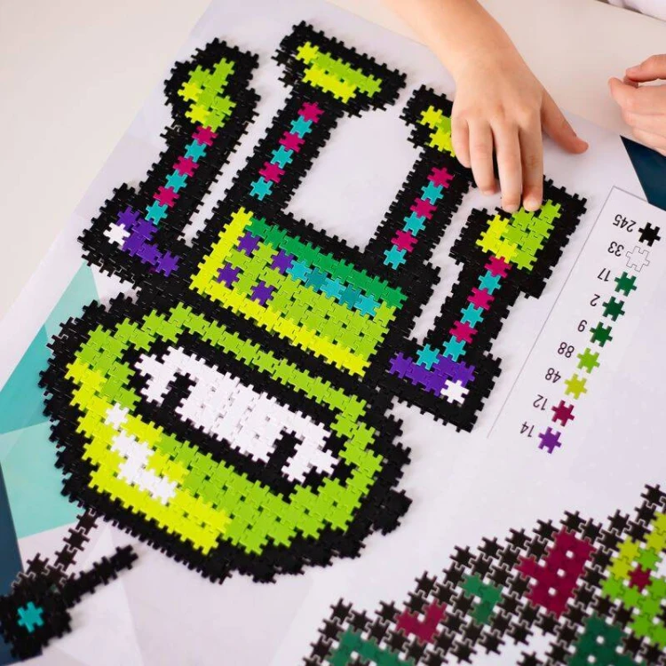Kolorowe elementy ułożone na rozkładanej planszy-instrukcji 69 × 48 cm, prezentacja wzoru w skali 1:1.