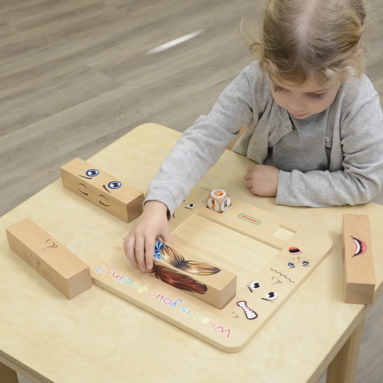 Komponenty ułożone w pudełku — drewniane elementy i karty z ikonami emocji z zestawu MASTERKIDZ